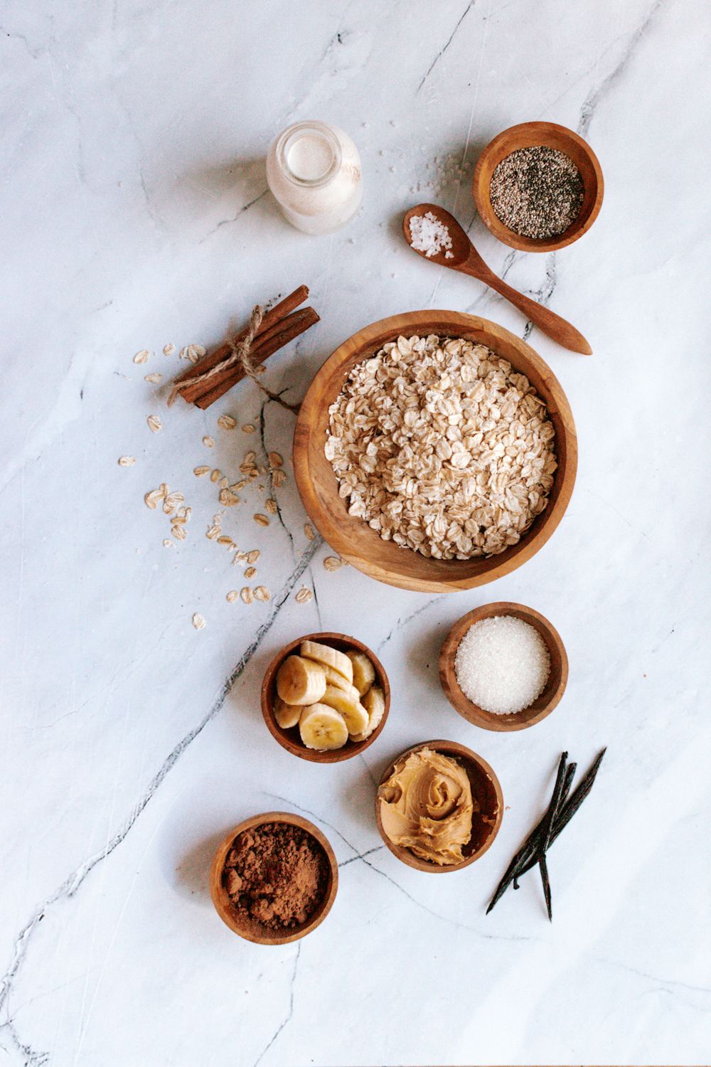 Ingredients for overnight oatmeal including rolled oats, cinnamon, banana, peanut butter, and cocoa powder.